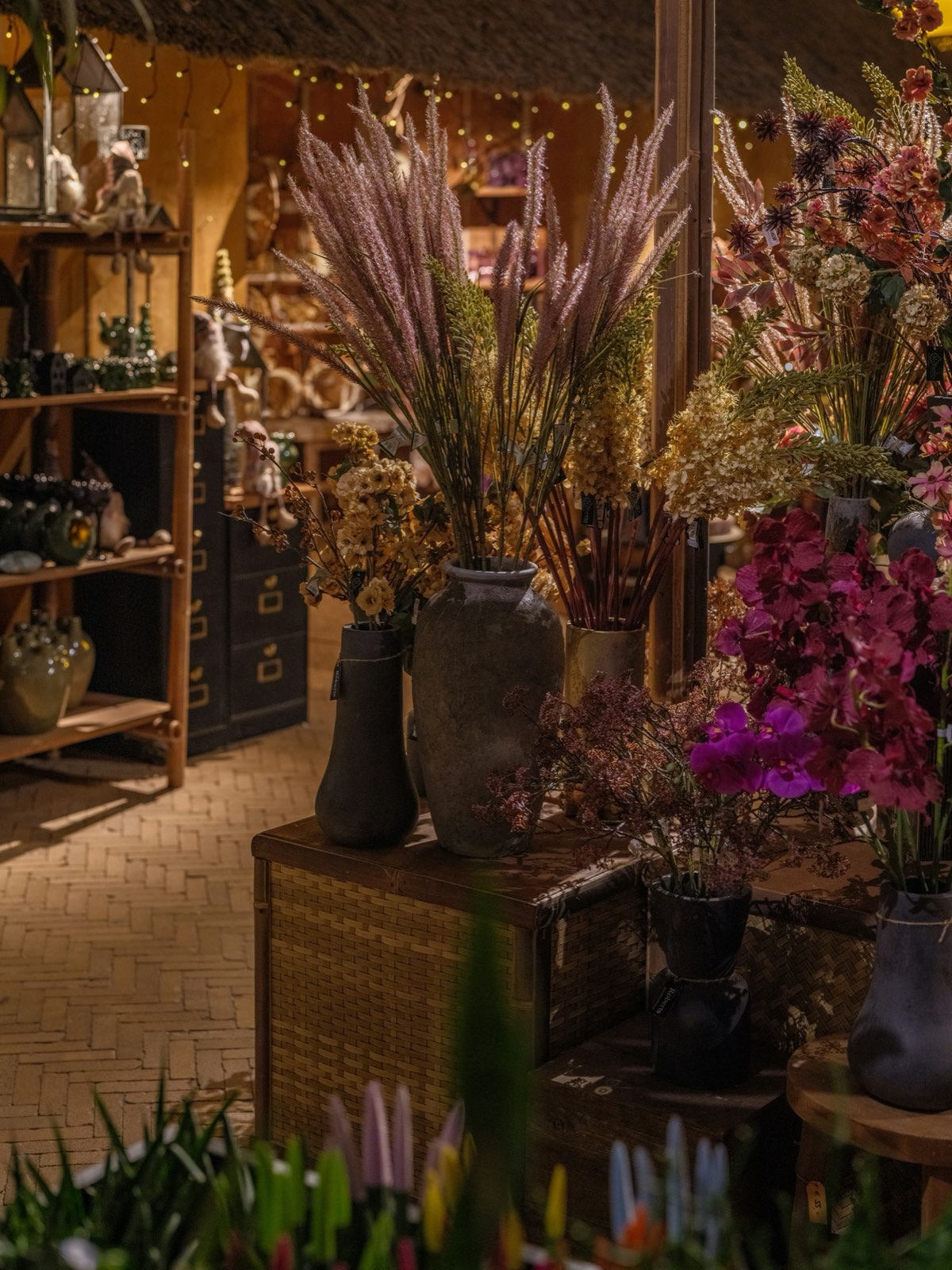 Interior cálido de un taller floral con jarrones, ramas secas y flores de temporada